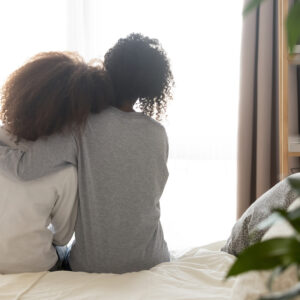 two women hugging on the edge of a bed